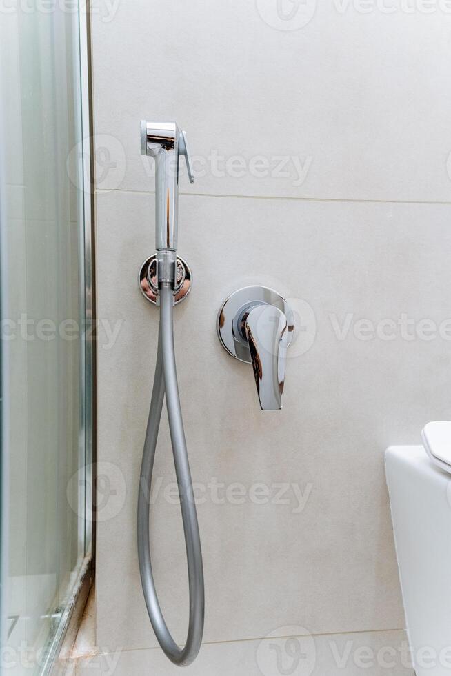 Common fixtures in a bathroom include a toilet and a wallmounted shower head which are essential for its functionality. Plumbing is crucial for ensuring fluid flow in the household photo