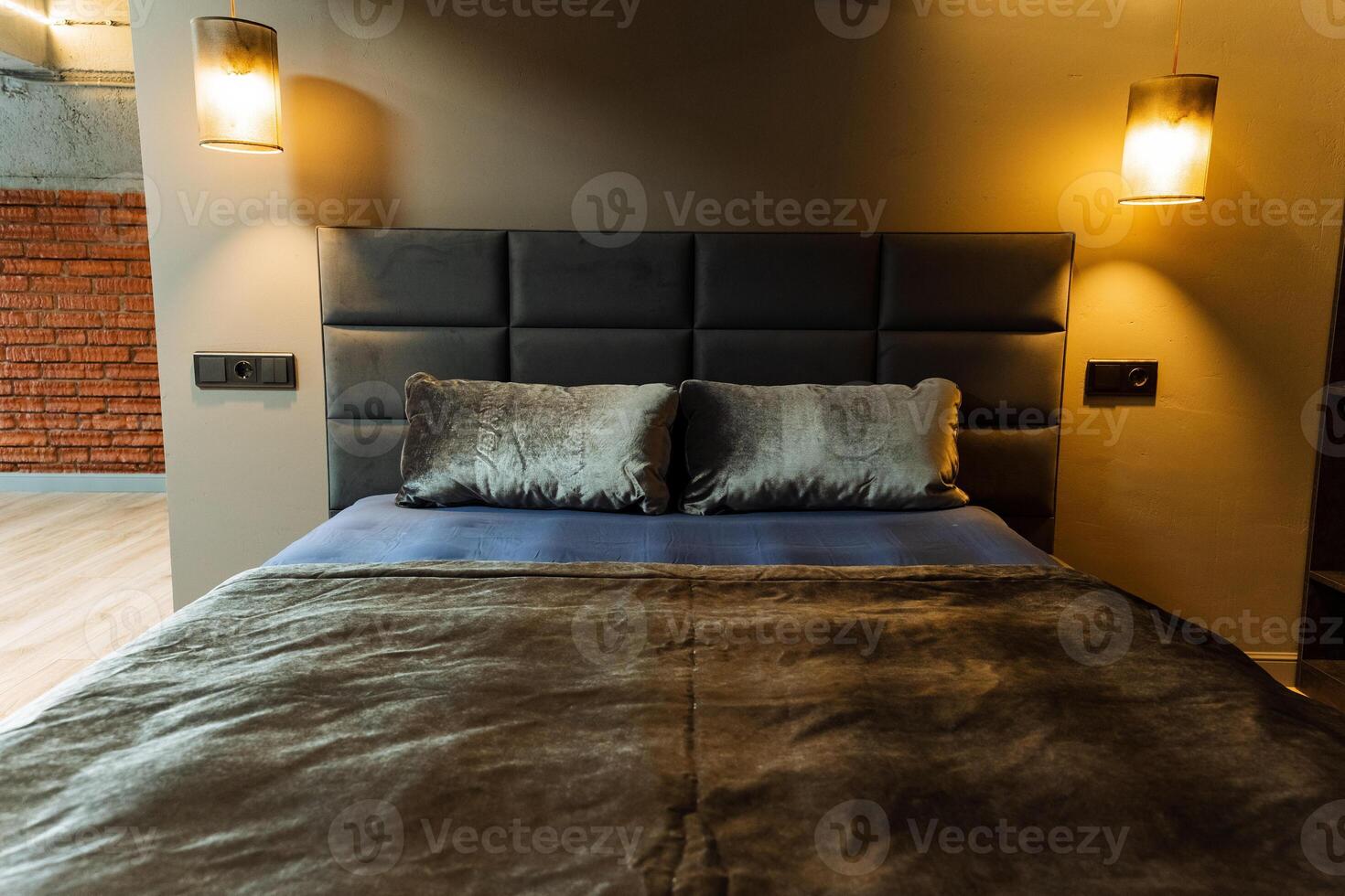 The room boasts a bed, a brick wall, wood flooring, a hardwood door, and a stained ceiling, all designed with a touch of interior design, creating a cozy and stylish ambiance photo