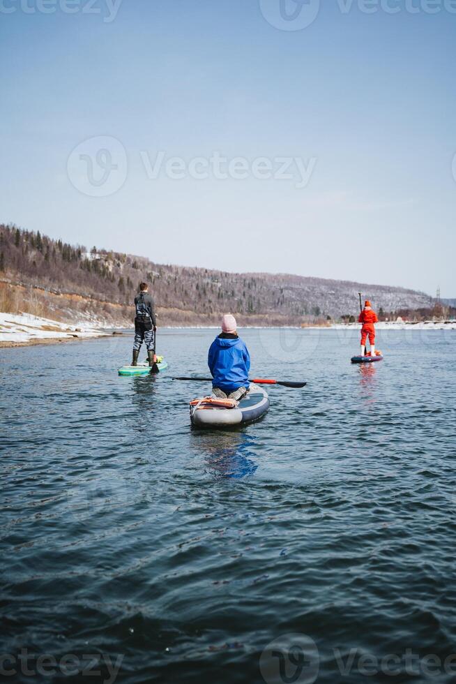 SUP boarders sailing on a mountain river, rear view of people standing on a board with a paddle, a team of athletes, outdoor activities on the water. photo