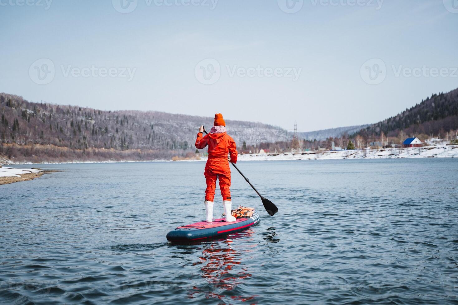 A woman stands on a SUP board and paddles, a man in a red protective suit floats on a board with a paddle on a mountain river, rear view. photo