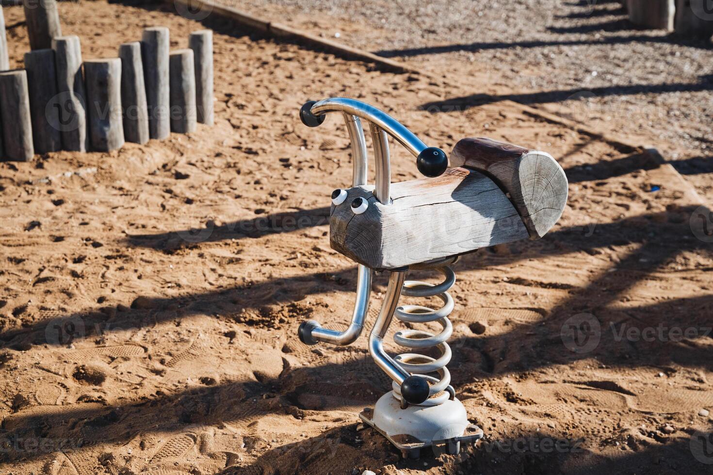 A beautifully crafted rocking horse can be seen sitting in the soft sand at a colorful playground, inviting children to come and play with it. Its a charming sight for all photo
