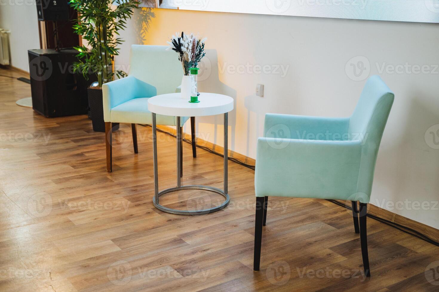 Two chairs next to a table with a vase of flowers in a building photo