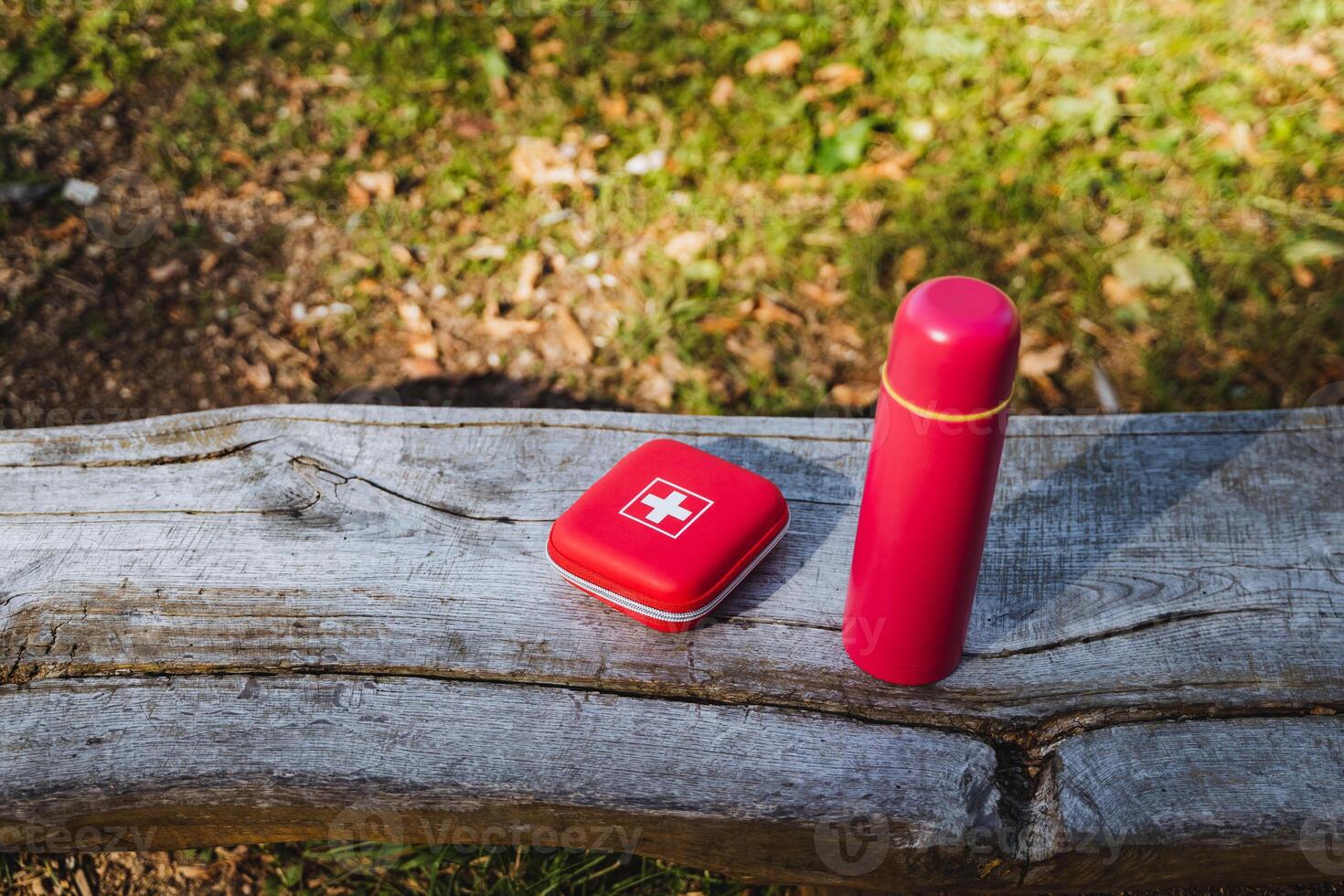 A sturdy wooden bench in a serene outdoor setting features a first aid kit and a red thermos, offering convenience for emergencies and refreshments during leisure activities photo