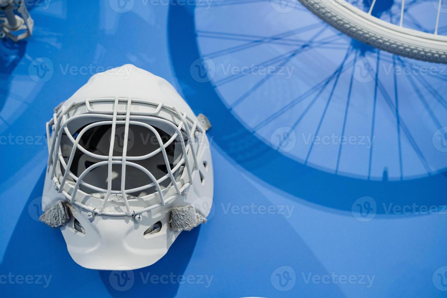 A hockey helmet is positioned on a vibrant blue surface right next to a bicycle wheel, forming a captivating contrast between two different kinds of sports equipment and cycling items photo