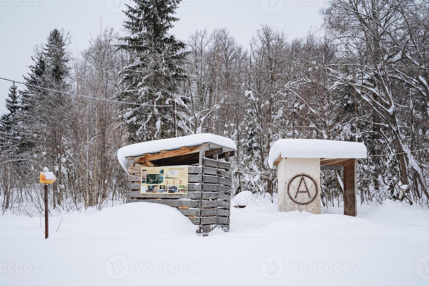 A delightful and charming wooden shelter is gracefully nestled deep in the very heart of a snowy forest, surrounded by majestic towering trees blanketed in pristine white snow photo