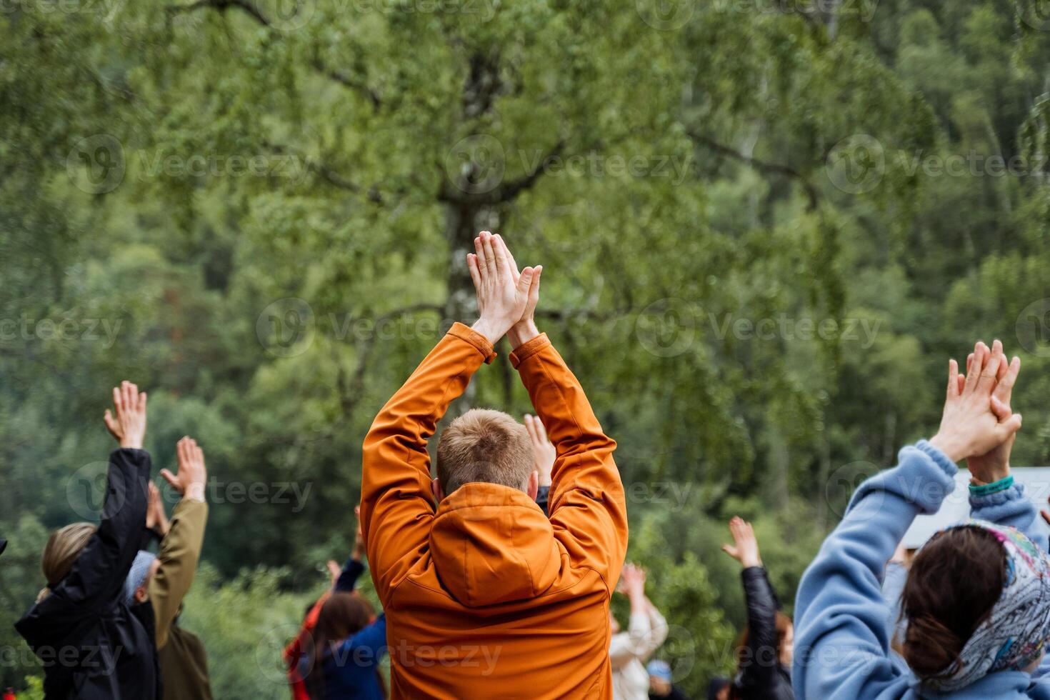 A group of people stand in a circle with raised hands, enjoying nature together surrounded by trees and grass, symbolizing leisure and unity in a natural landscape setting photo