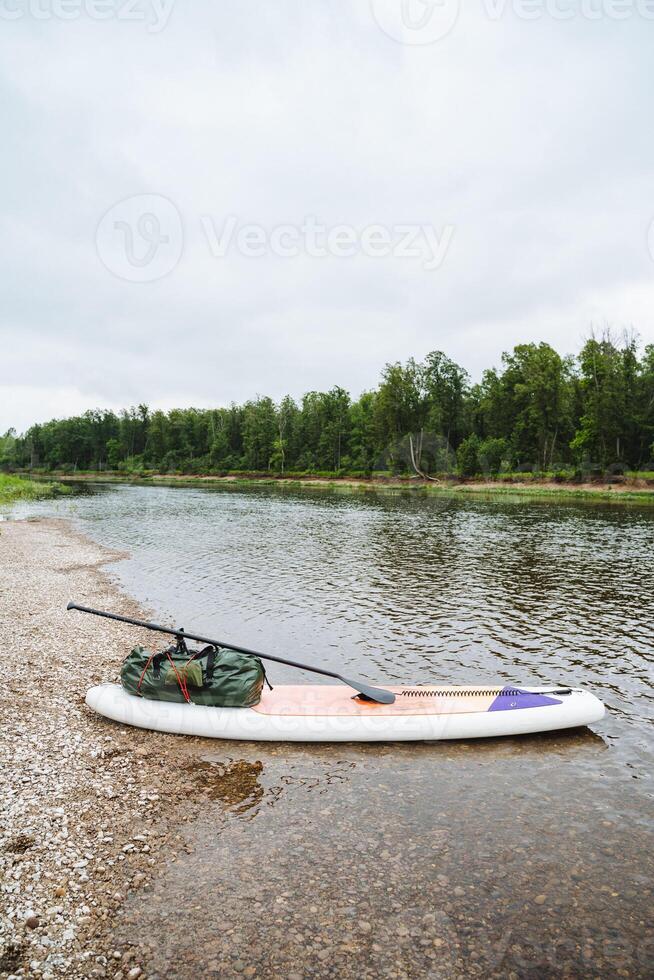 A tranquil image of a paddle board gliding on a peaceful riverbank, embraced by abundant greenery under a serene sky, reflecting the serenity and natural beauty of the surroundings photo