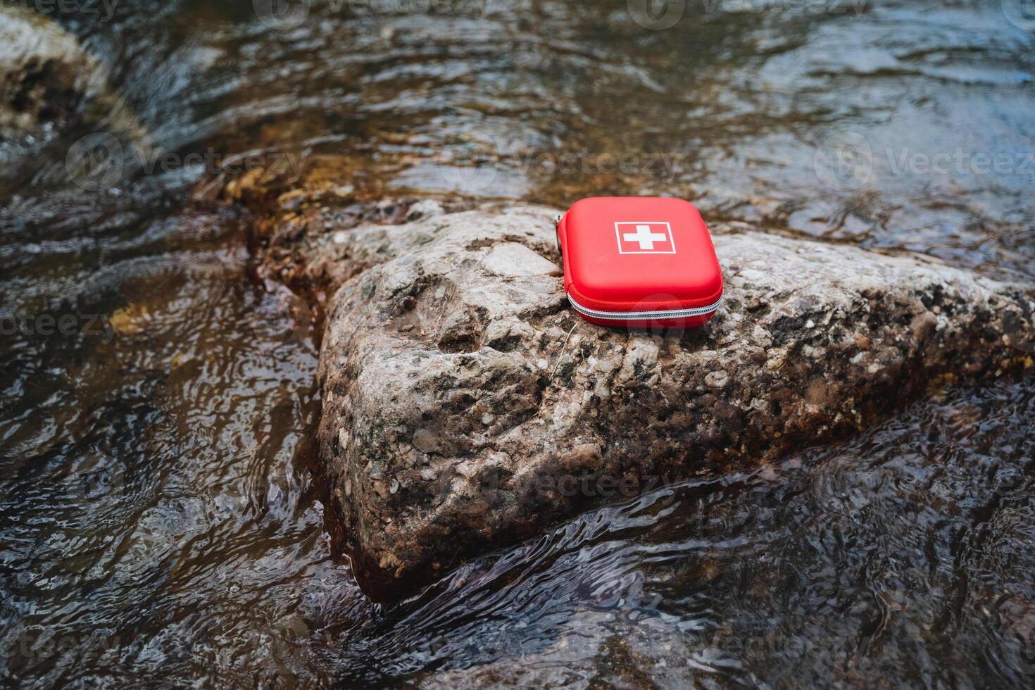 A red first aid kit placed on a rock in a flowing stream, symbolizing emergency preparedness, outdoor safety, and the importance of health and safety in natural environments photo