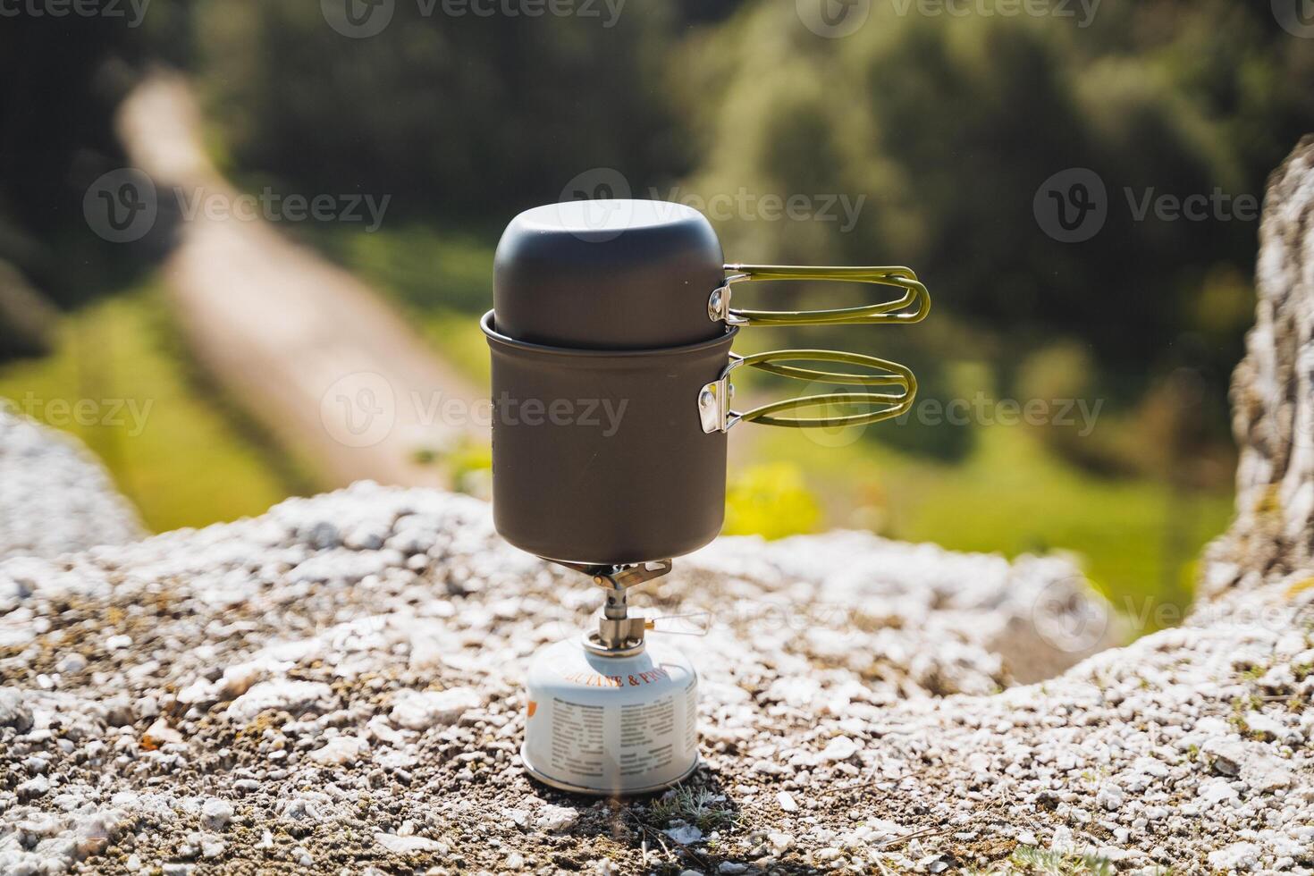 A small cooking pot is situating itself atop a tiny stove resting on a rock photo