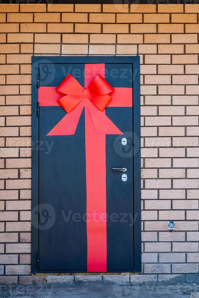 The charming red bow on the striking black door stands out against brickwork, creating a captivating feature in a balanced design. The door becomes a standout element in the setting photo