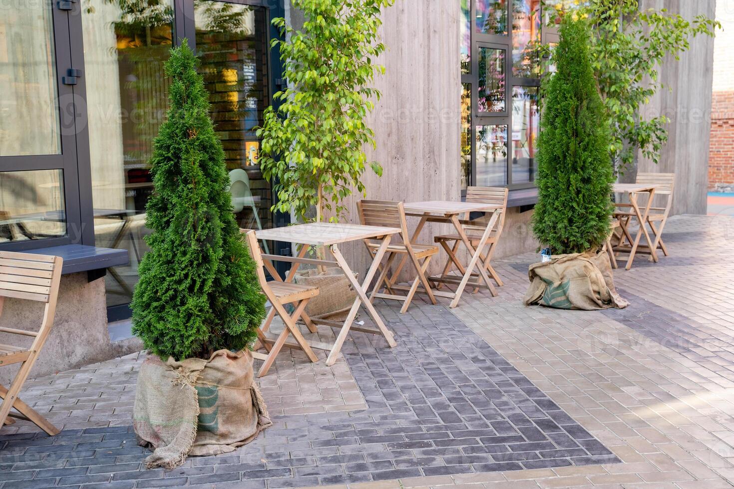 There is a long row of tables and chairs placed outside, with green trees standing in front of a charming building, creating a pleasant and inviting atmosphere for visitors photo