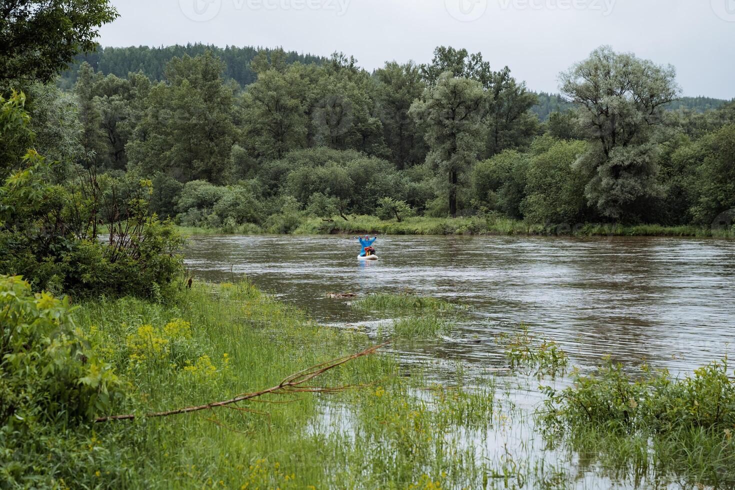 An idyllic scene of a figure in a blue kayak leisurely navigating through a tranquil river surrounded by verdant trees, showcasing the allure of nature and aquatic activities photo