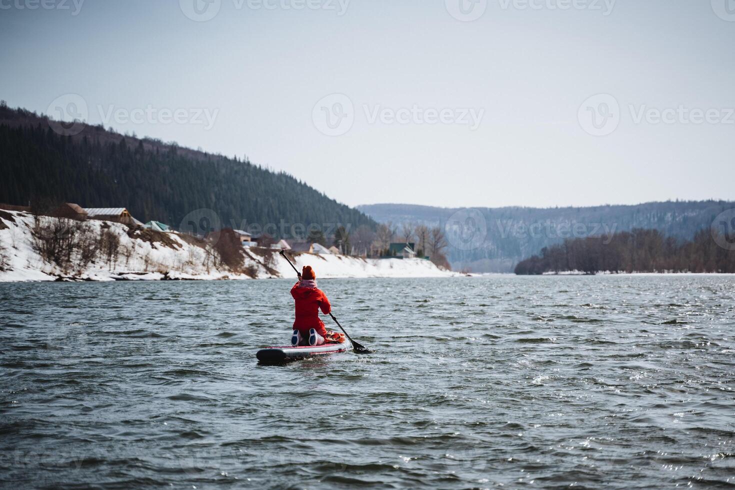 A SUP boarder paddles along a river against the background of mountains, a man sits on a board and travels on a mountain lake, a hiking trip in spring on Fode. photo