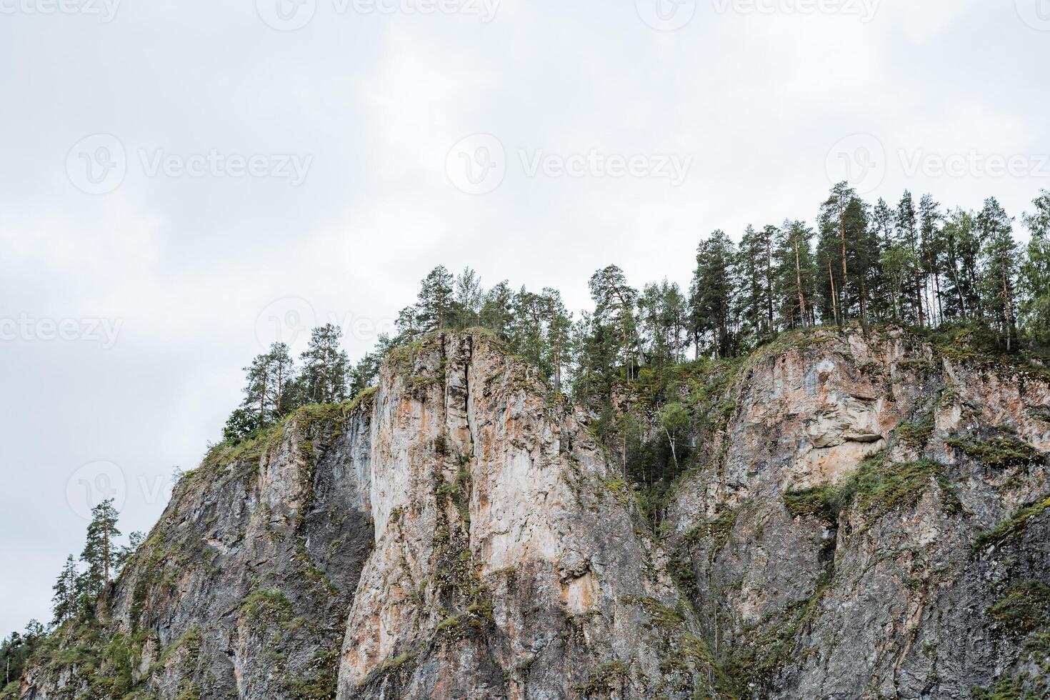 A mountainous outcrop covered in dense trees under a cloudy sky, creating a serene natural landscape with terrestrial plants and a peaceful atmosphere. It depicts the beauty of nature photo