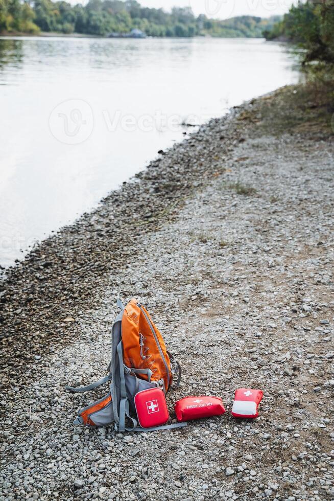 On the beach, adjacent to a flowing river, there is a backpack resting alongside some first aid kits, indicating readiness for adventure and exploration in the great outdoors photo