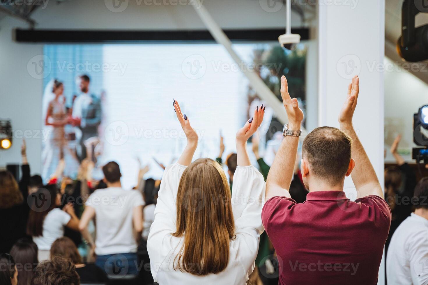 Crowd raising hands in gesture of fun at entertainment event with large screen photo