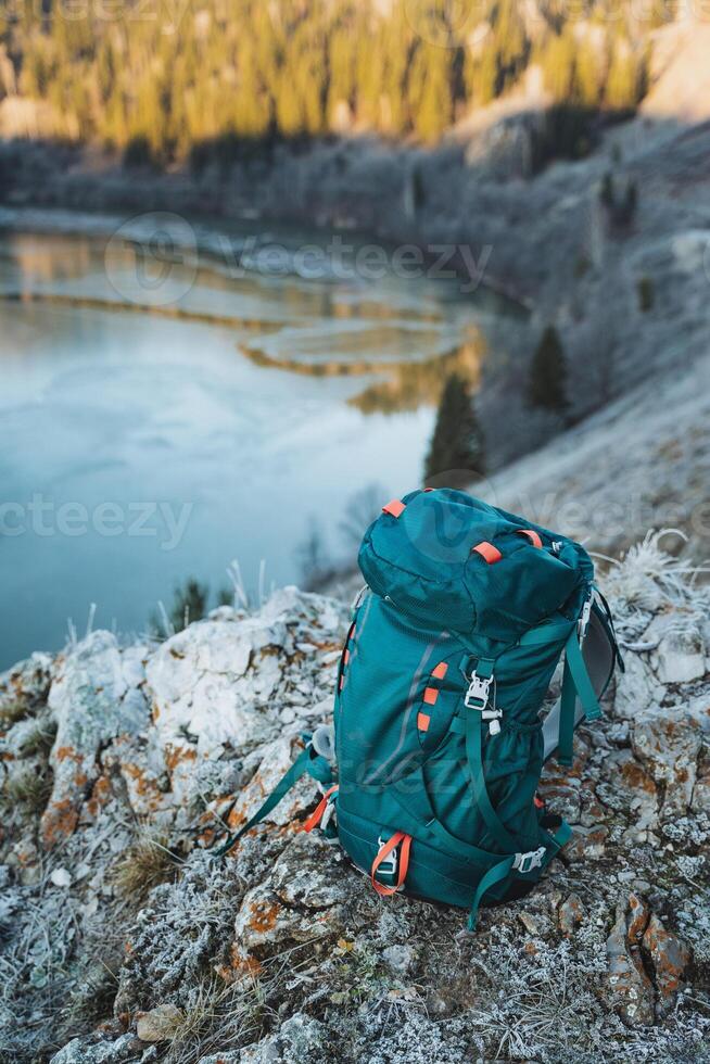 A tourist backpack stands on a stone against the background of a mountain lake, camping equipment, a bag for things. photo