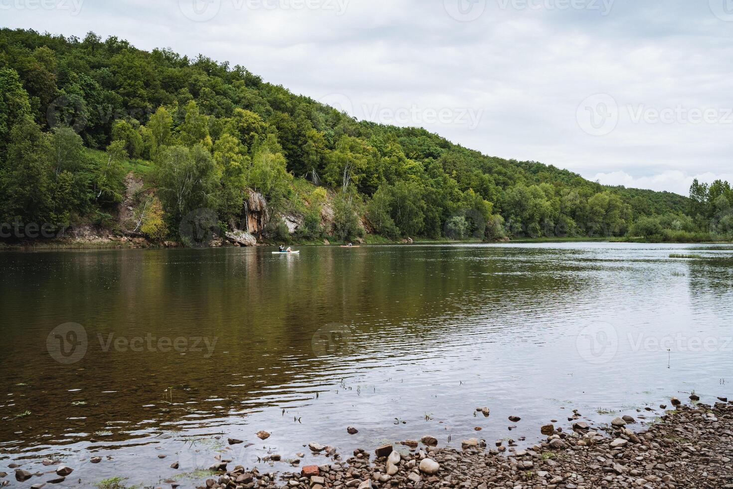 The tranquil river setting, surrounded by a forest and rocky shore, offers a serene and picturesque view of natures beauty, ideal for finding peace and tranquility photo