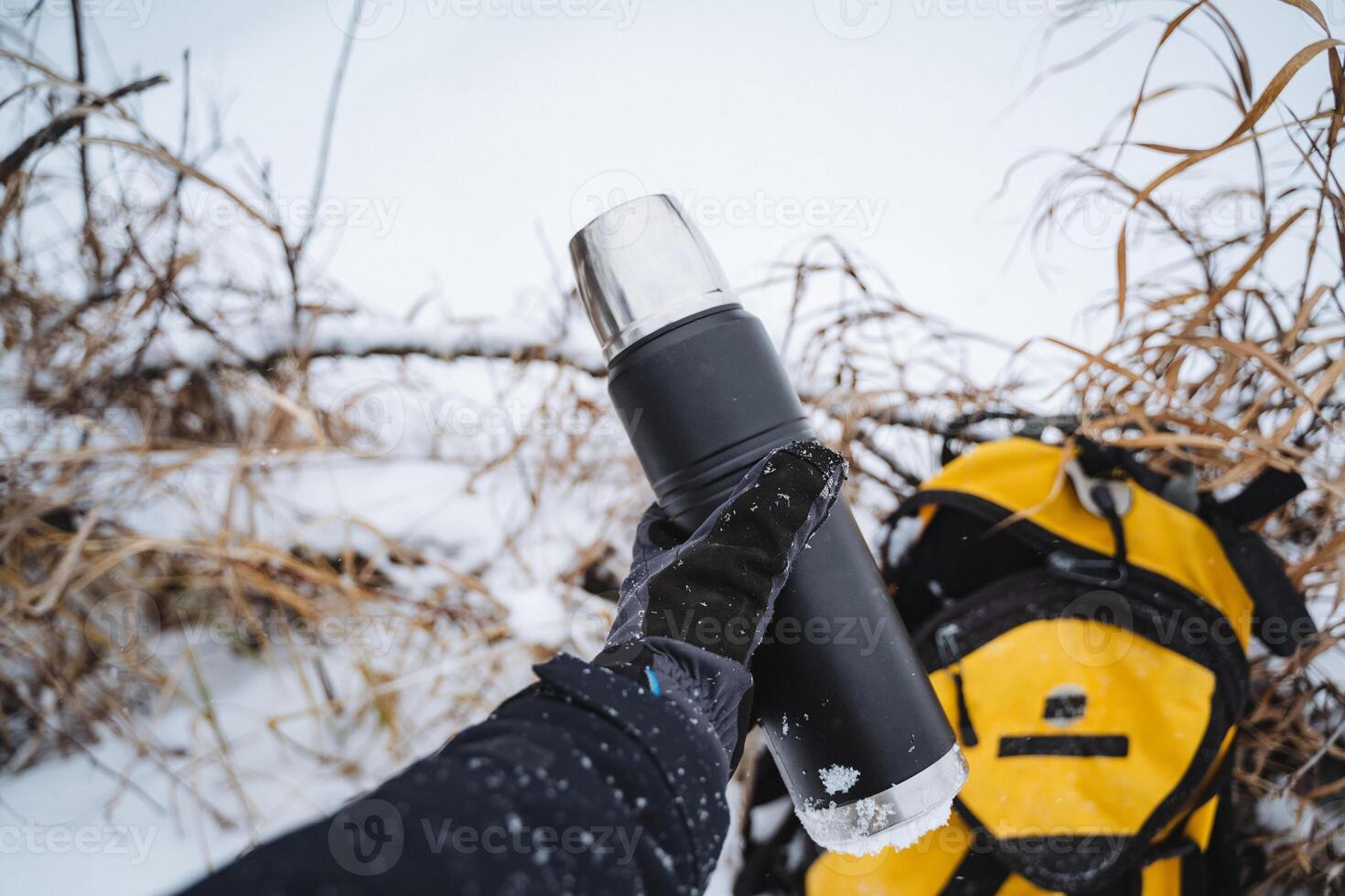 A person tightly grips a thermos while standing amid the snow, ensuring that its warm contents maintain a comfortable temperature despite the frigid and freezing environment around them photo