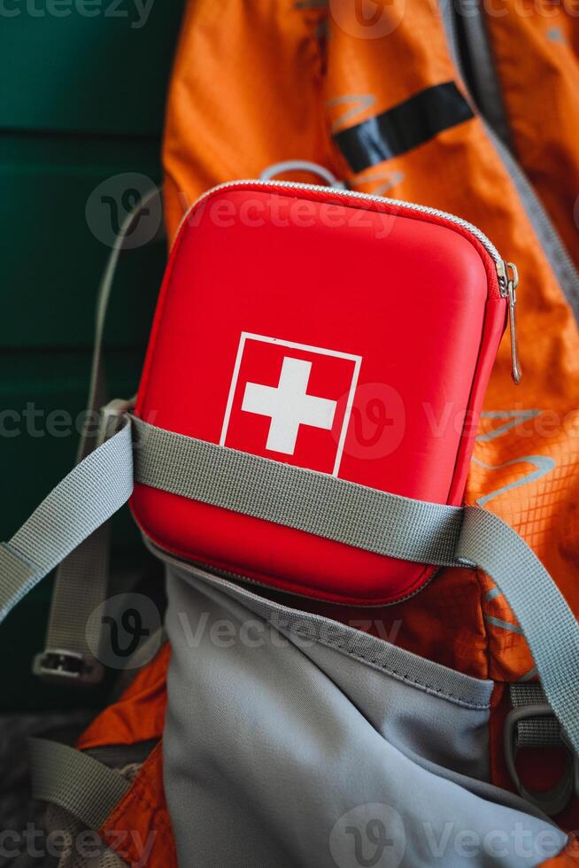 Inside a backpack, there lies a bright red first aid kit that features a prominent white cross symbol, designed to ensure easy access during emergencies and various outdoor activities photo