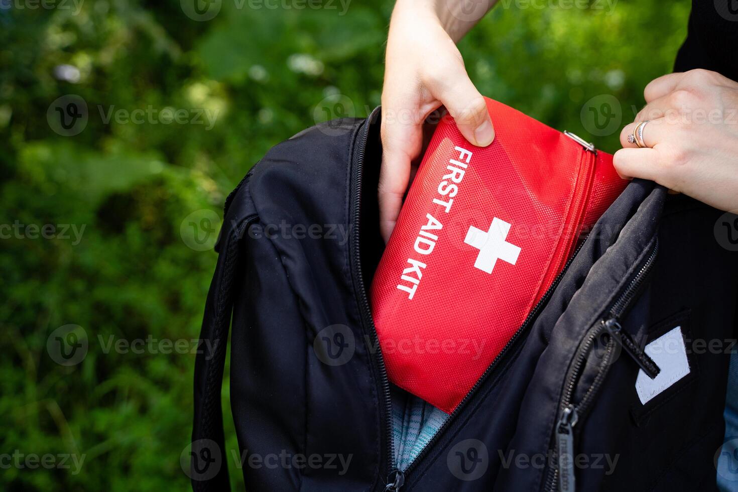 A person is carefully placing a first aid kit into their backpack while preparing for an upcoming journey or travel event, ensuring they are equipped for any potential emergencies photo