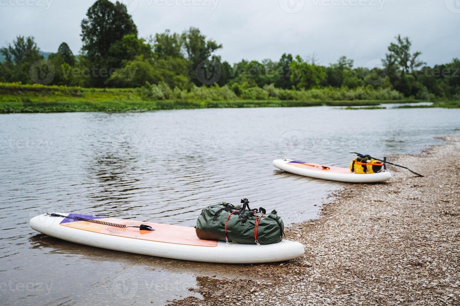 A picturesque riverbank depicts paddle boards and camping gear, inviting outdoor adventures in a serene setting, perfect for relaxation and exploration in nature photo