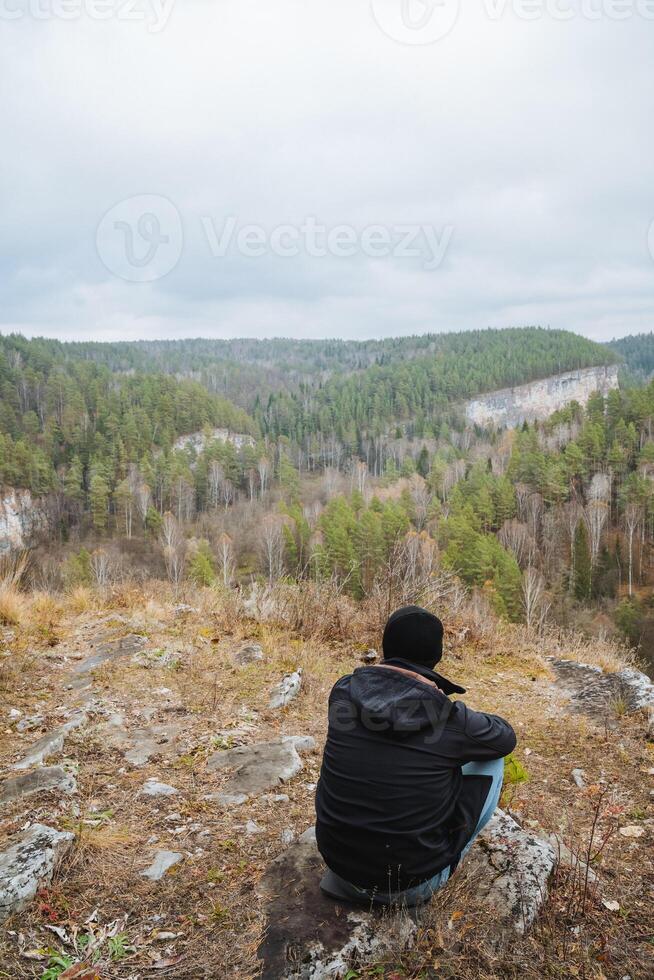 A man is peacefully sitting atop a rock while he gazes out over the expansive valley in front of him, taking in all the beauty of his natural surroundings and the landscape photo
