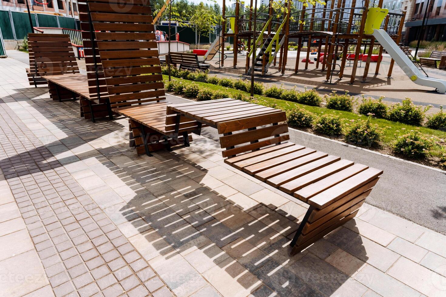 Wooden benches in the park create a serene atmosphere with a playground in the background, offering a tranquil setting for visitors to relax and enjoy nature while surrounded by greenery photo