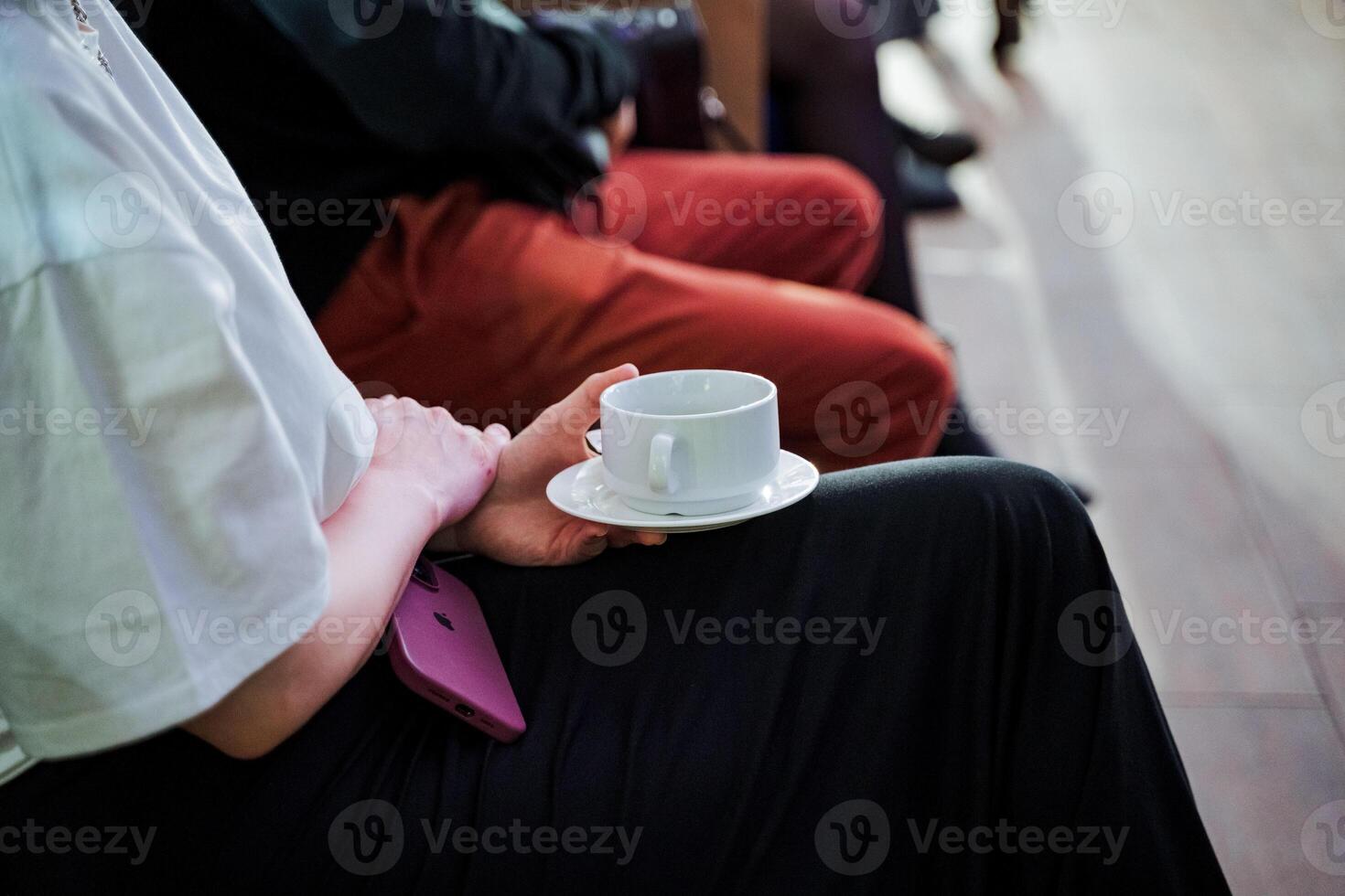 Person holding a coffee cup on a saucer with their thumb and finger photo