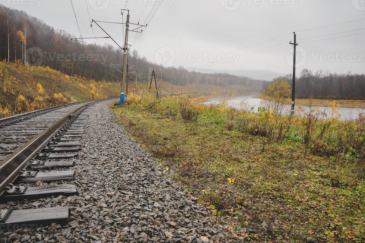 Train track cuts through field with river, trees, and clouds in background photo