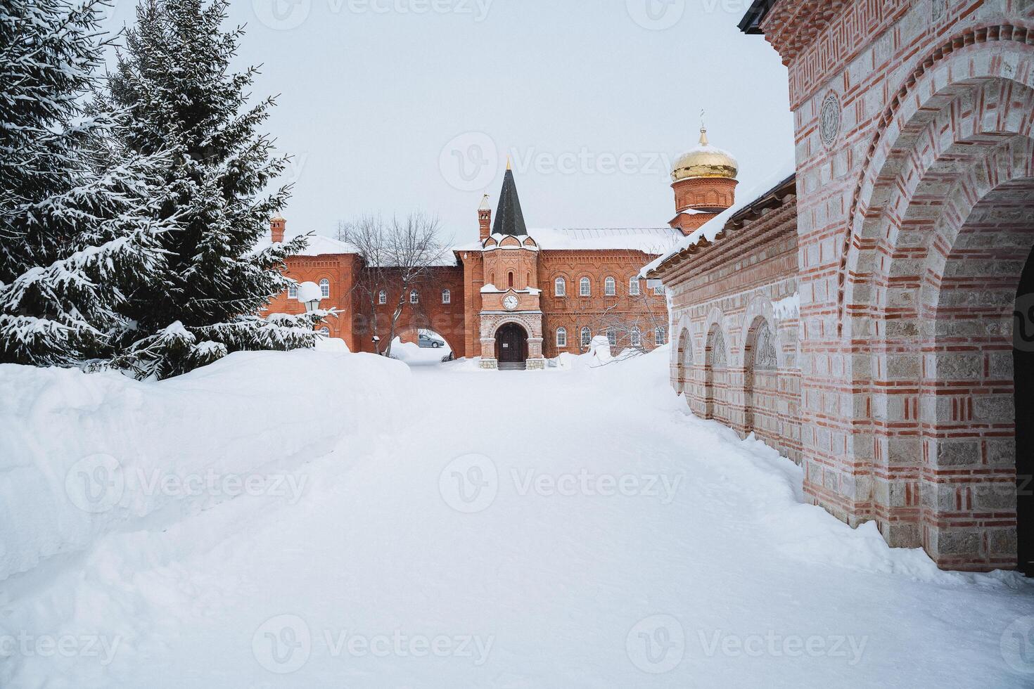 a snowy path leading to a brick building with a tower in the background photo