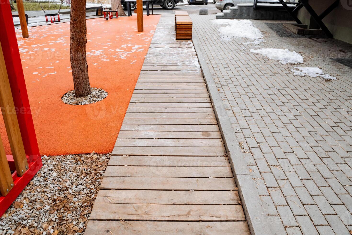 A wooden walkway gracefully directs visitors towards a playground that is located at the center, with a beautiful tree standing tall in the middle, creating a natural setting for play photo