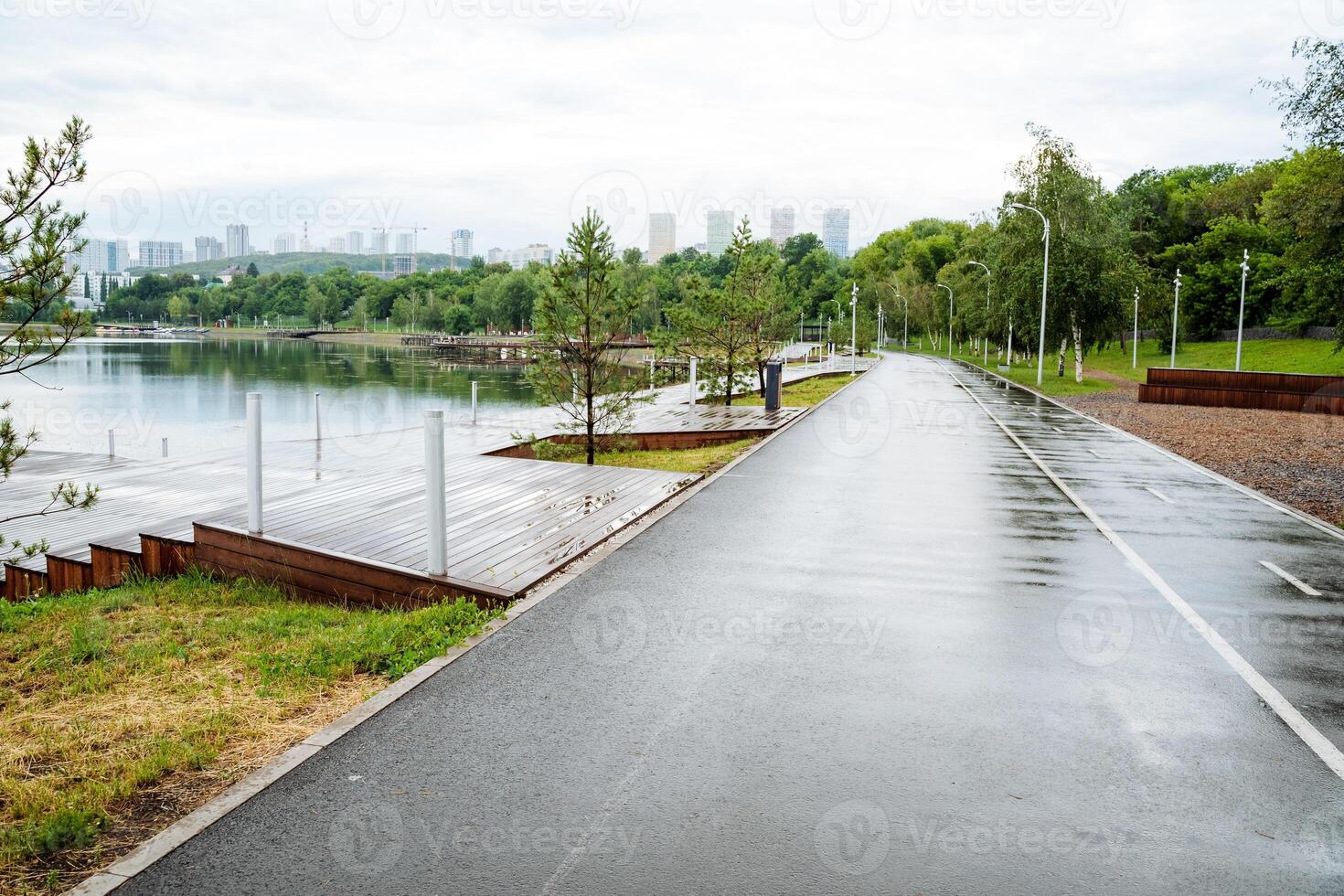 An empty park pathway is wet by the waterfront on a cloudy day, offering a serene environment for leisure with a scenic view, a perfect place to enjoy nature and unwind photo