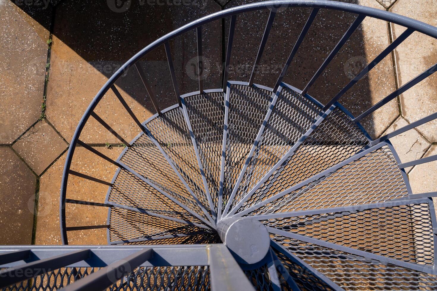 Aerial view of a beautifully designed spiral staircase with a mesh design and textured ground surface beneath photo