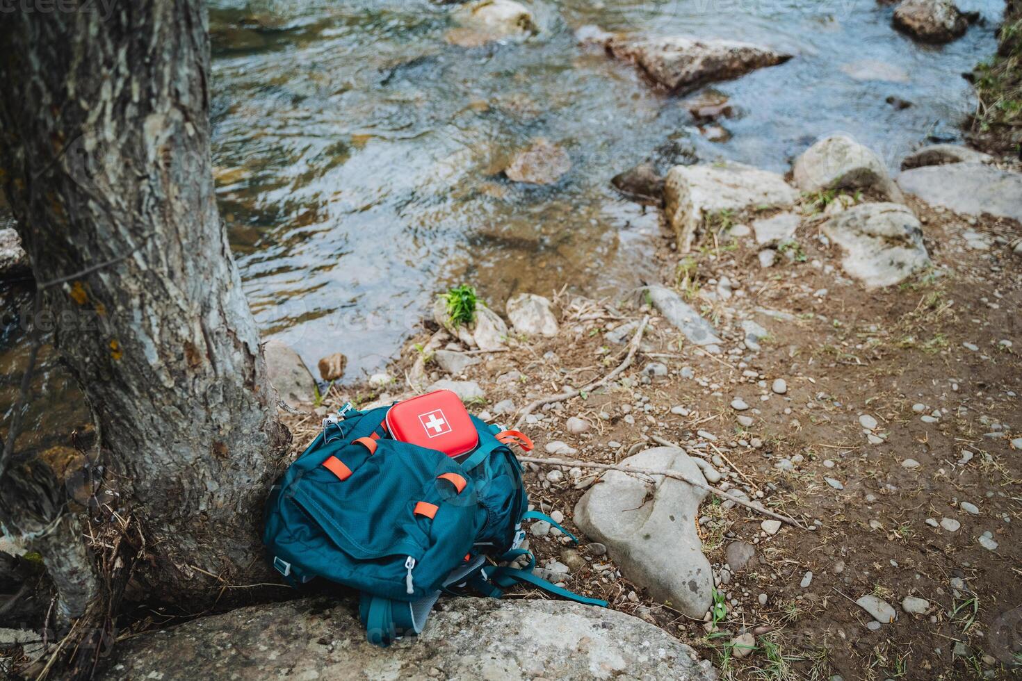 An electric blue backpack is resting on a rock by the river in the jungle. It sits on soil in the polluted landscape, a plastic fashion accessory and personal protective equipment photo