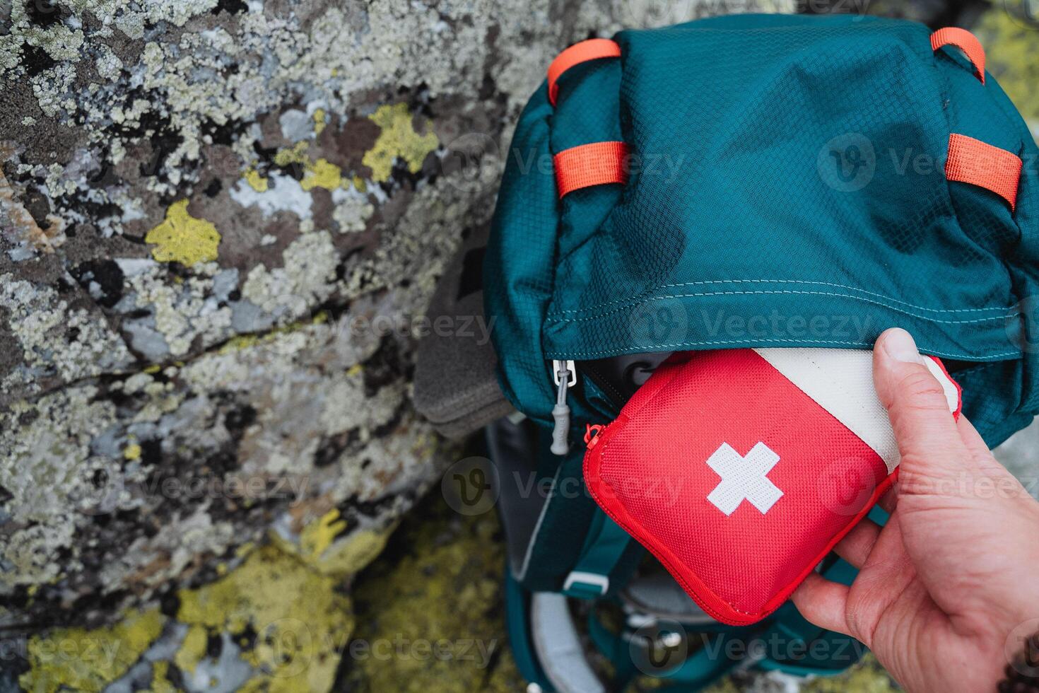 Hand taking out first aid kit from hiking backpack, red first aid kit on a journey, concept of an autonomous hike in the forest. photo