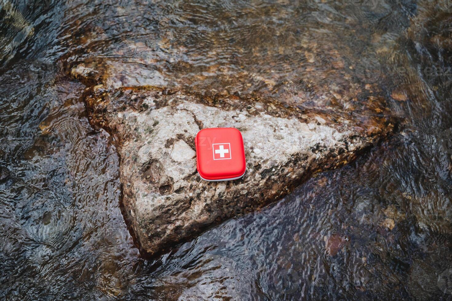 Red first aid kit for emergency medical care in the outdoors. Ideal for rocky surfaces in streams or rough terrain. Essential for wilderness survival and adventure photo
