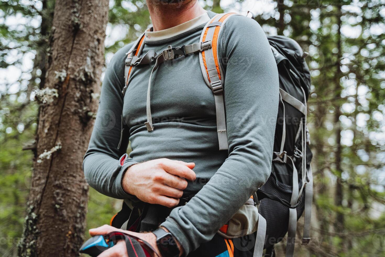 A man wearing sportswear and sunglasses stands in the woods with a backpack photo