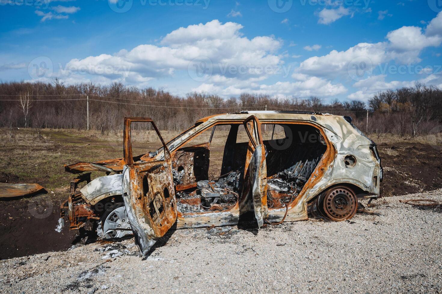 The open doors of a car burned down after a crash on the road, the car is standing in a field against the background of a blue sky. photo