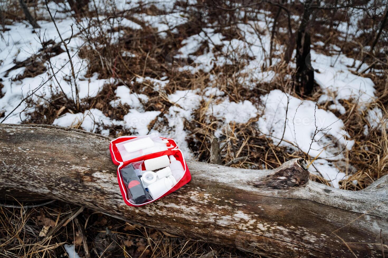 A first aid kit is positioned on a log that rests in the snow, showcasing the stark contrast between the warm colors of the kit and the cold, white landscape surrounding it photo