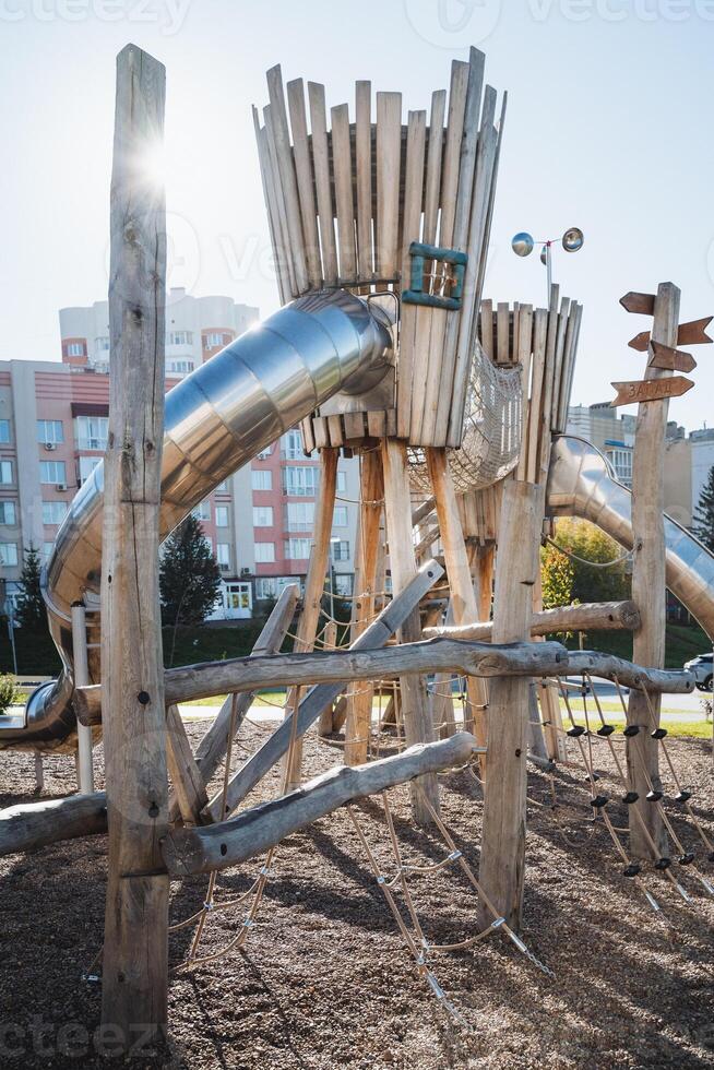 A delightful wooden playground featuring a colorful slide right in the center, surrounded by trees and grass, creating a fun space for children to play and enjoy their time outdoors photo