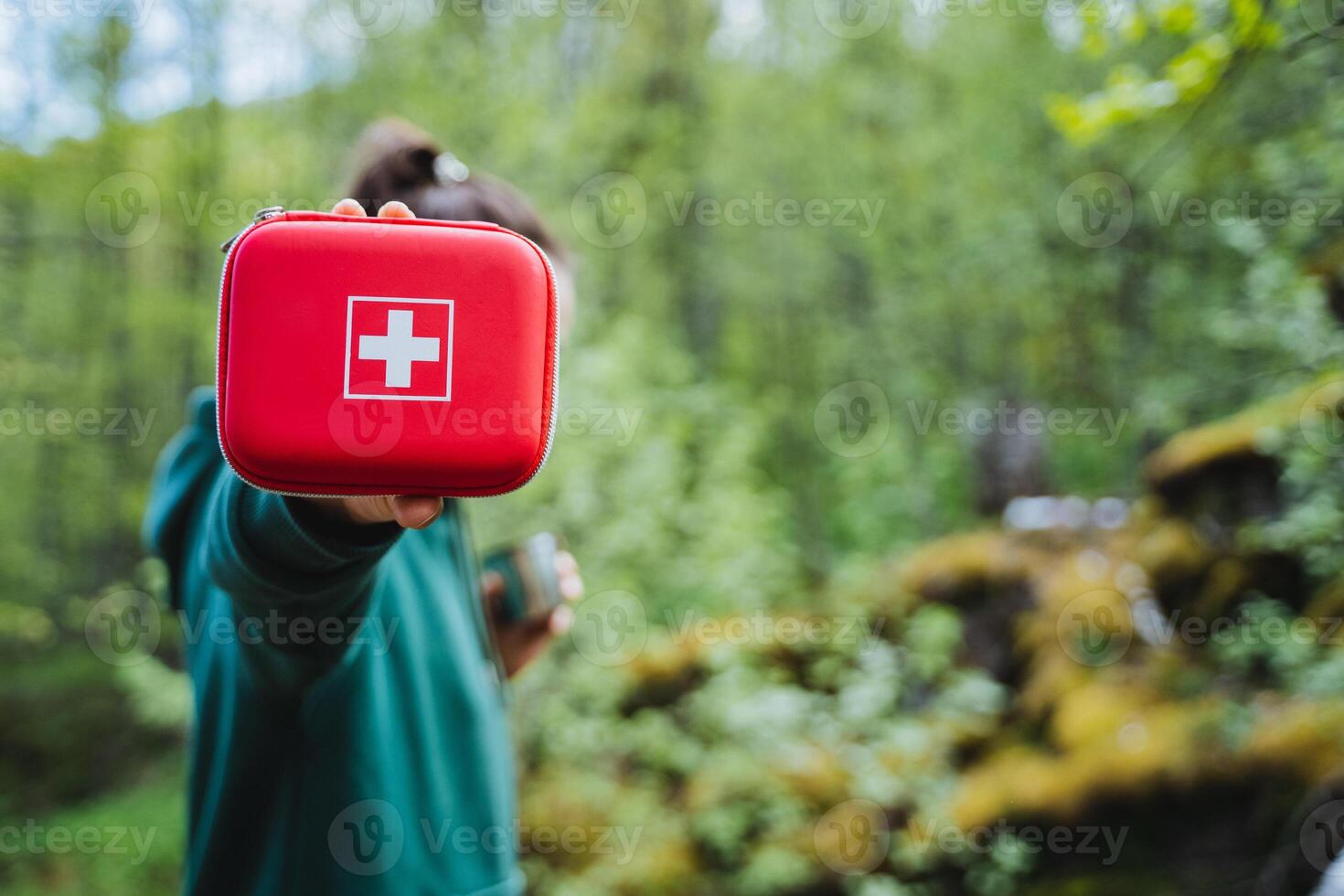 Man with red first aid kit promotes outdoor safety in lush forest. Be prepared for emergencies during hiking or camping with essential medical supplies and equipment photo
