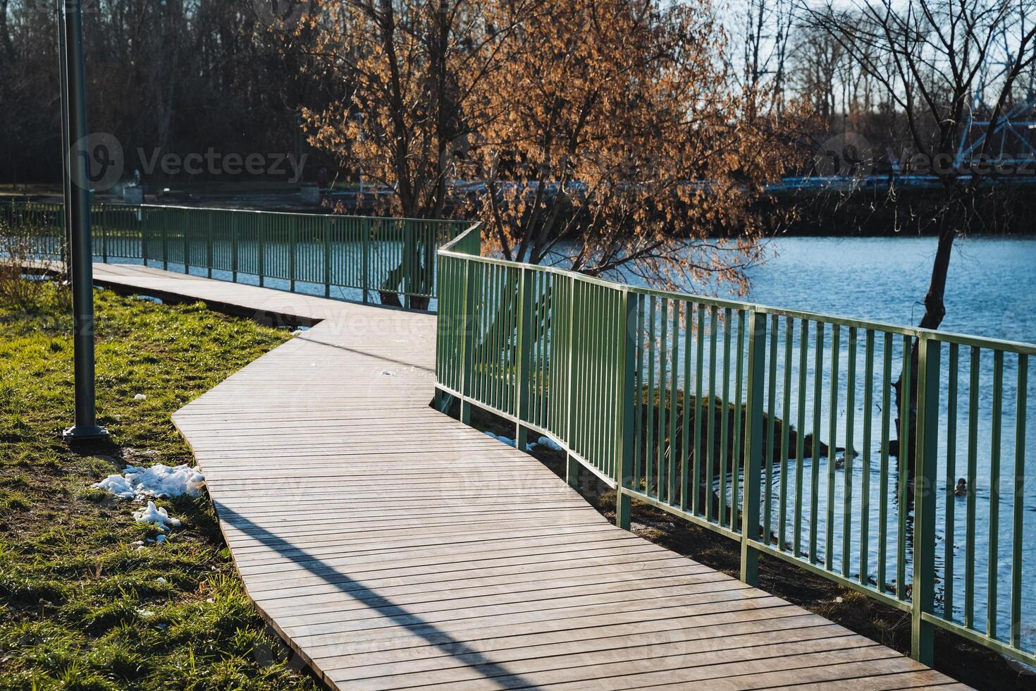 A wooden walkway leading to a lake with a green fence photo