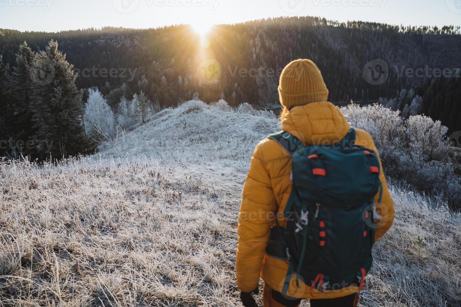 Man with backpack traveling in the mountains in winter view from the back, trekking in the mountains at dawn of the day, hiking in nature in December, glare of the sun over the mountain. photo