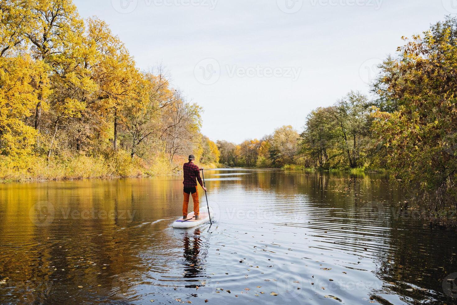 A man is skillfully maneuvering a paddle board on a picturesque river, fully immersing himself in the serene surroundings while appreciating the stunning beauty of nature all around him photo