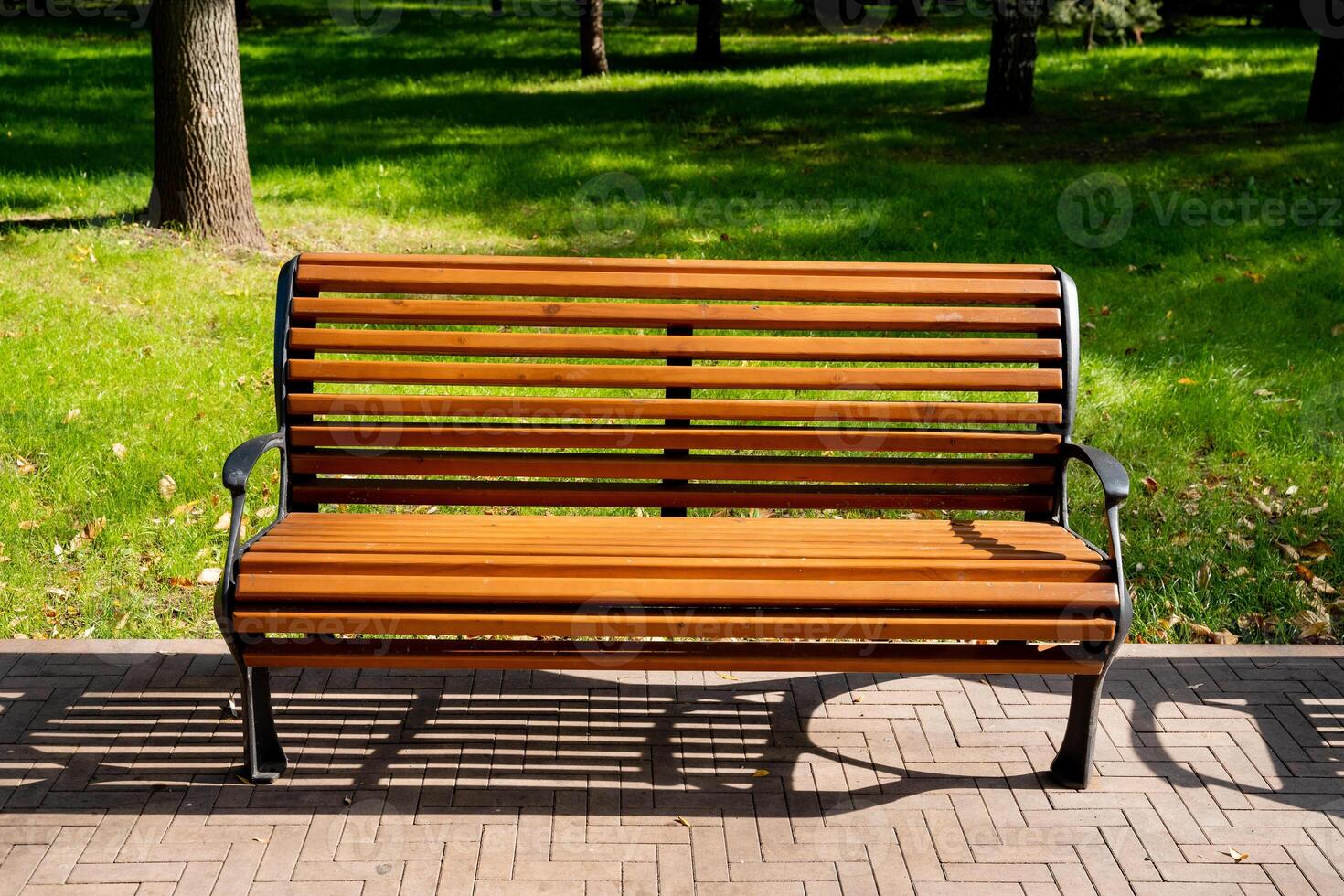 A beautifully crafted wooden park bench is comfortably situated on a meticulously maintained brick sidewalk nestled within the serene and tranquil environment of a picturesque park setting photo