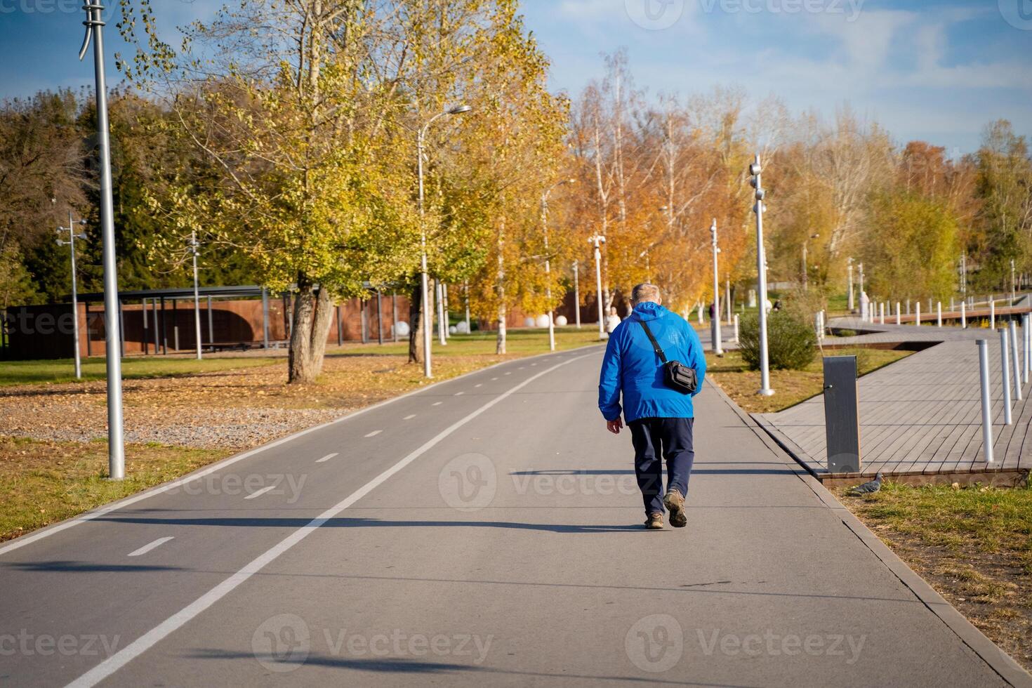 A man dressed in a stylish blue jacket takes a leisurely stroll along a picturesque park path, savoring the refreshing air and appreciating the lovely natural surroundings that embrace him photo