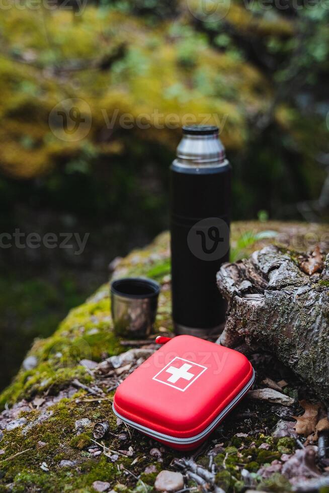 A first aid kit and a thermos rest on a rock in a grassy natural landscape photo