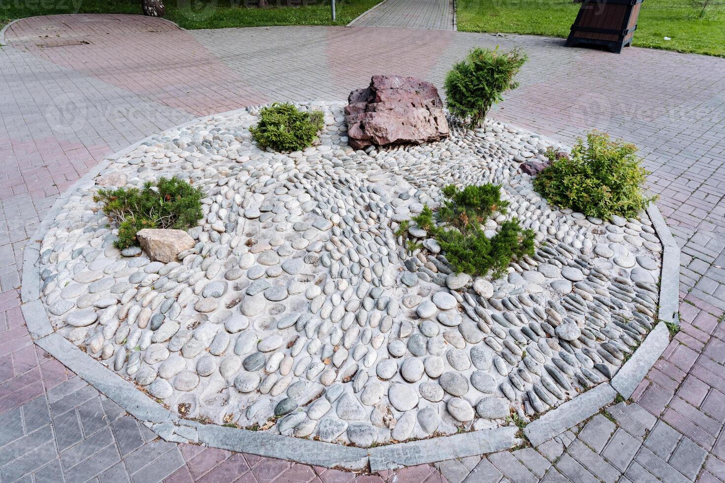 In an urban setting, a circle of rocks and plants on a brick sidewalk enhances the environment with natural beauty and greenery, creating a lovely focal point in the city landscape photo