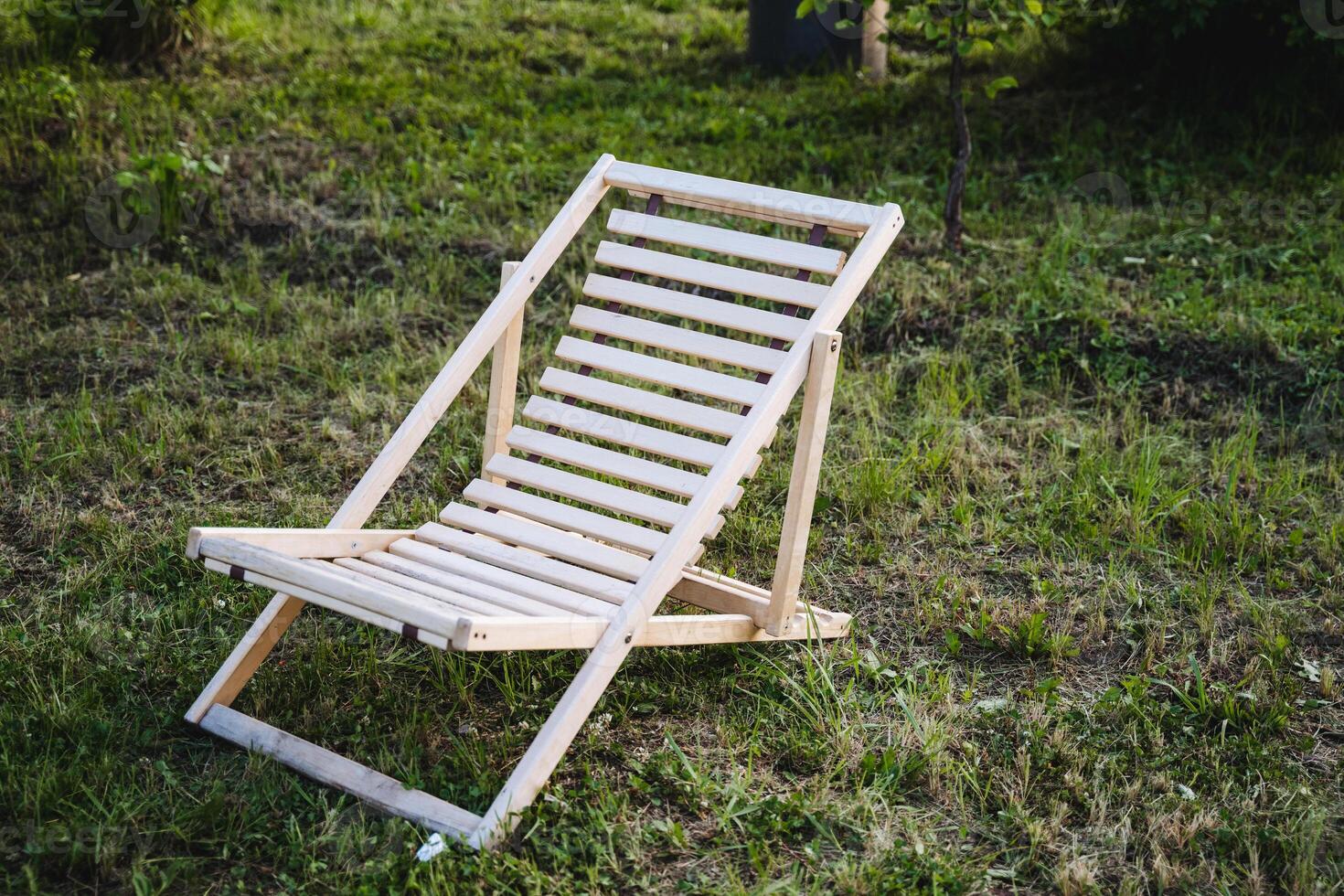 Set in a stunning outdoor location surrounded by greenery, a wooden deck chair is positioned for relaxation and comfort in a calm setting, ideal for leisure and enjoyment photo